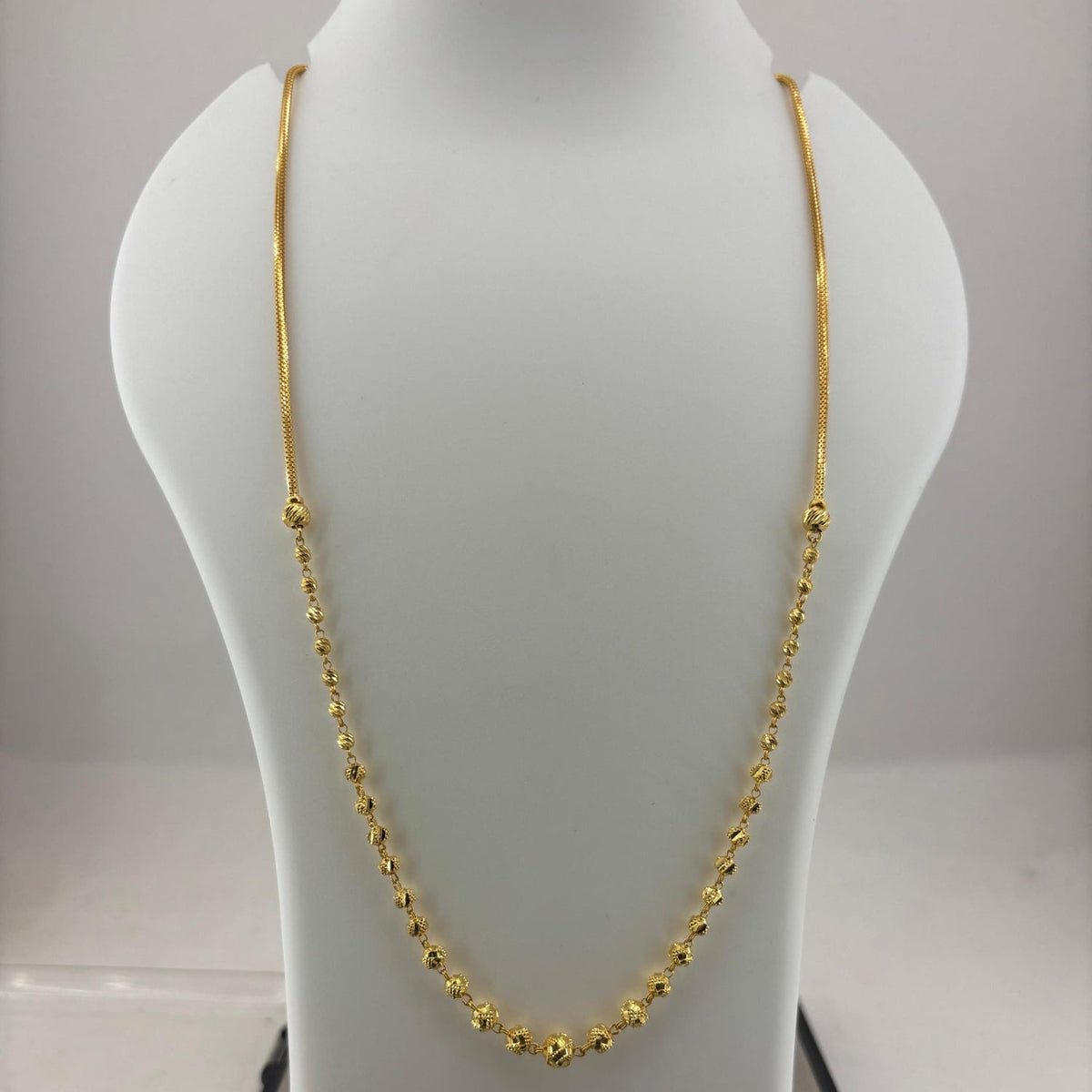 A gold chain necklace displayed on a white mannequin bust, with a digital scale visible underneath.