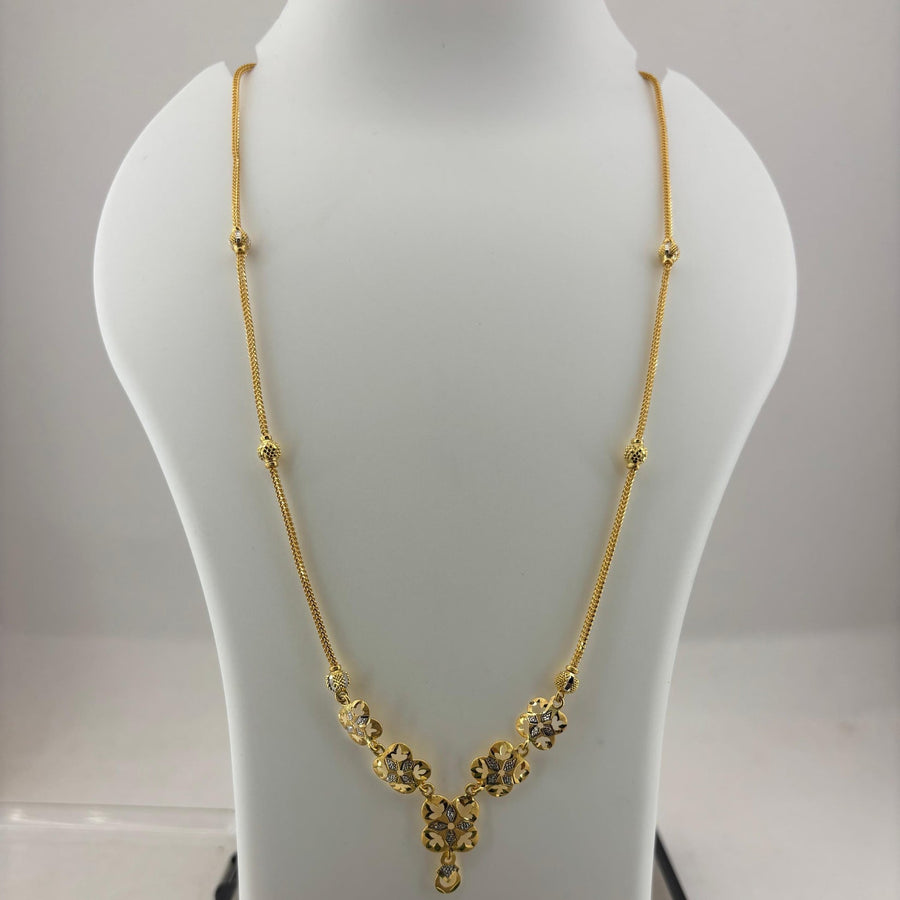 A gold necklace displayed on a white mannequin bust, with a digital scale visible underneath. The necklace features a delicate chain with small bead accents and a V-shaped pendant with floral clusters and a teardrop charm.