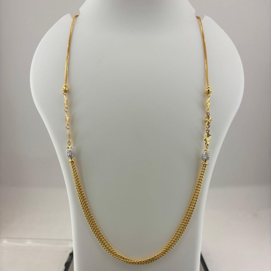 A gold chain necklace with small bead details and clear spacer beads, displayed on a white mannequin bust with a digital scale underneath.