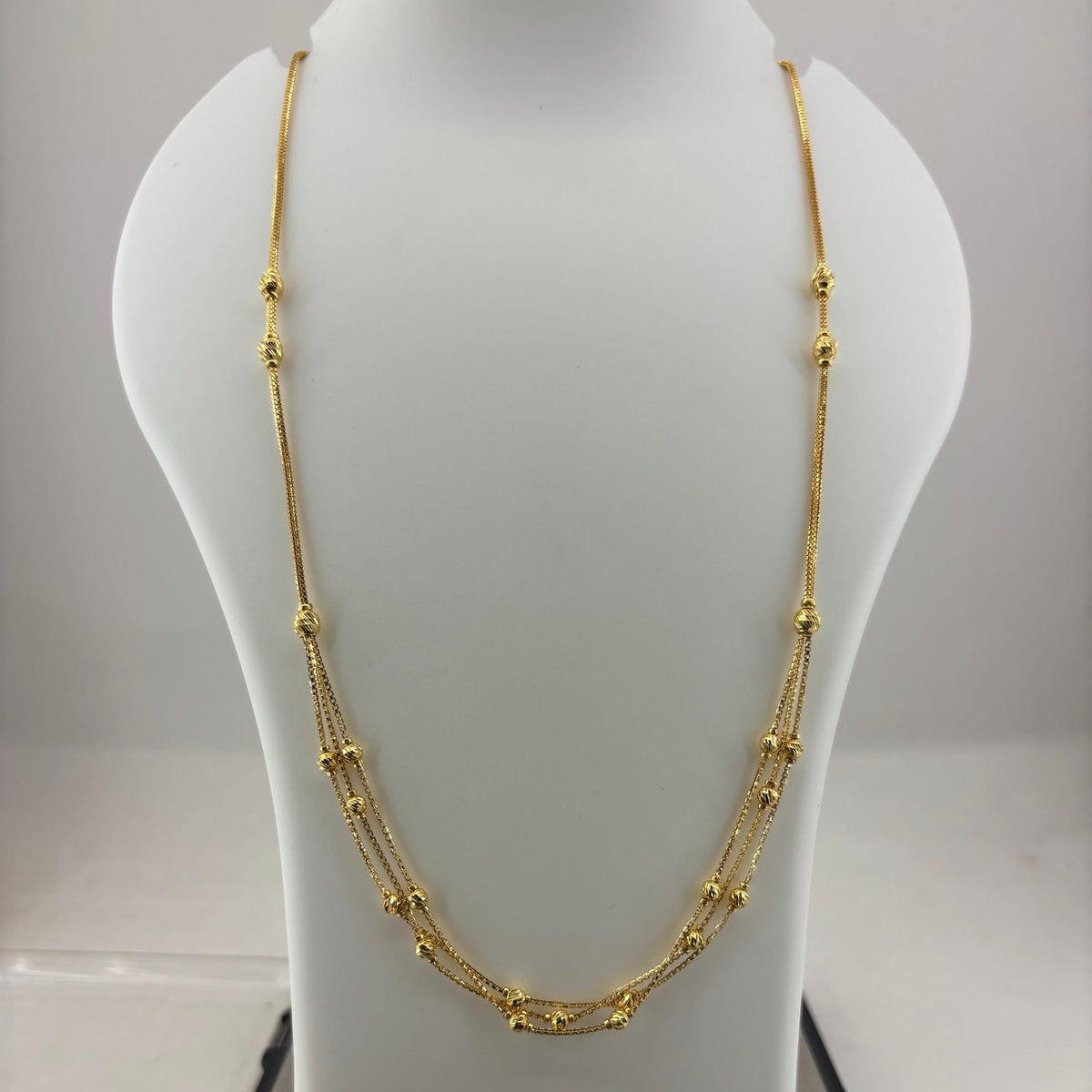 A gold multi-strand beaded necklace displayed on a white mannequin bust, with a digital scale visible underneath.