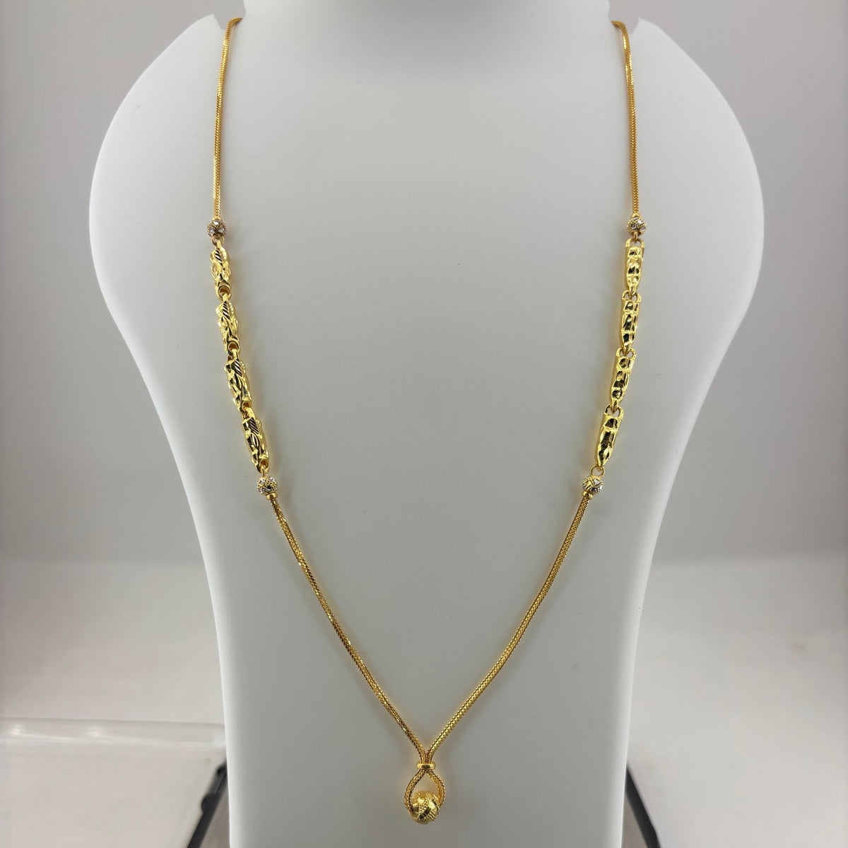 A gold necklace with a teardrop pendant displayed on a white mannequin bust, with a digital scale underneath showing a weight of 8.14 grams.