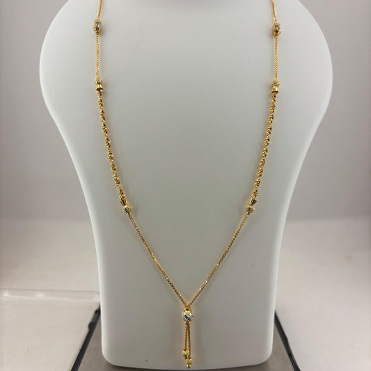 A gold necklace displayed on a white jewelry bust, with a digital scale visible underneath. The necklace has a delicate chain with small bead details and a central pendant with a clear stone.