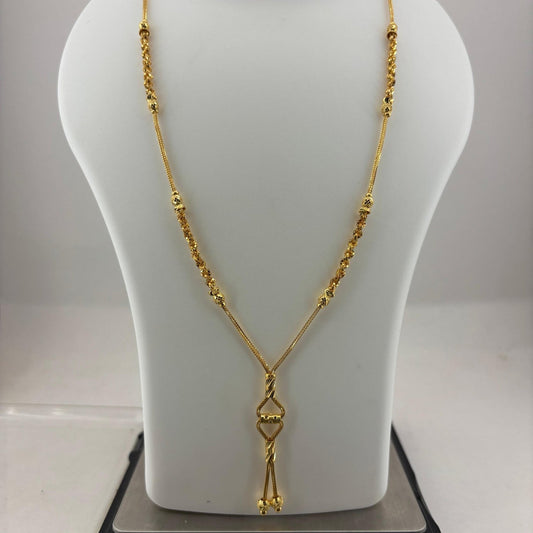 A gold necklace displayed on a white jewelry bust, with a digital scale underneath to show weight. The necklace features a textured chain and a pendant with a small central heart-shaped detail.