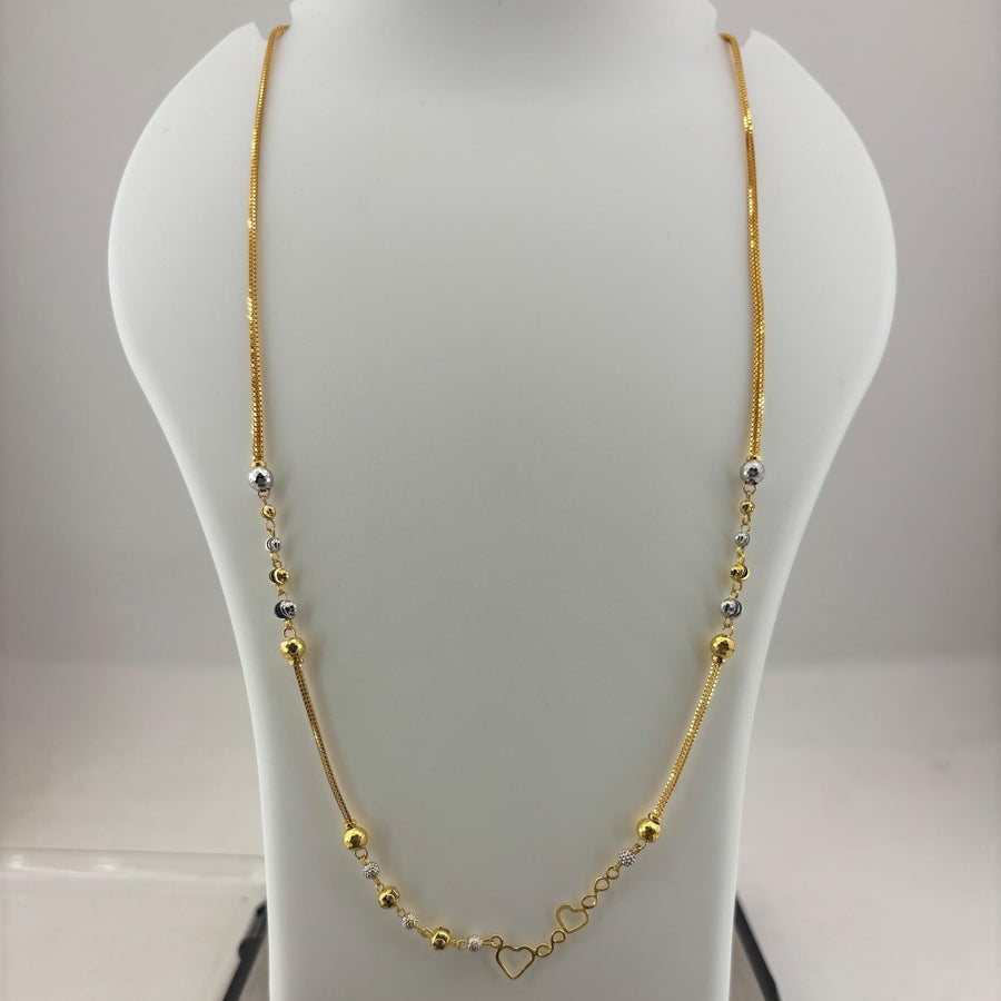 A gold necklace with small silver and gold beads and a heart-shaped clasp, displayed on a white jewelry bust sitting on a digital scale.