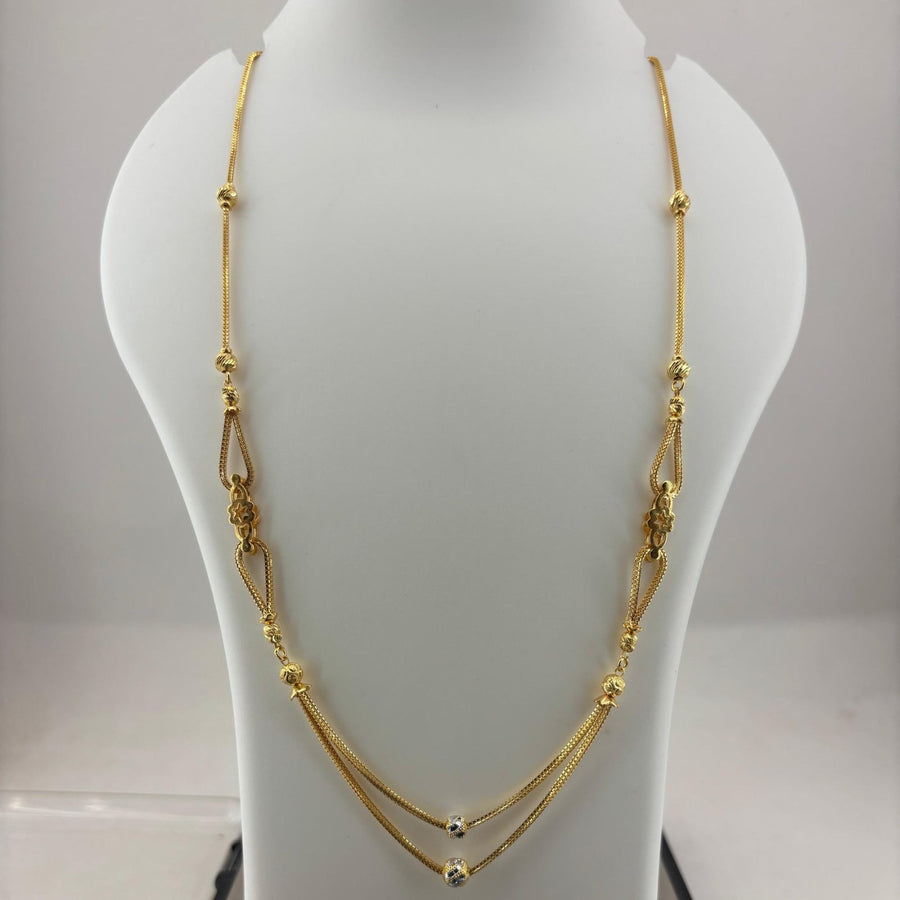 A gold-toned multi-strand necklace with textured bead details, displayed on a white jewelry bust stand with a digital scale underneath.