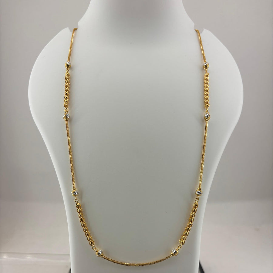 A gold chain necklace displayed on a white mannequin bust, with a digital scale visible underneath. The necklace features a smooth curved section at the bottom and small bead details spaced along the chain.