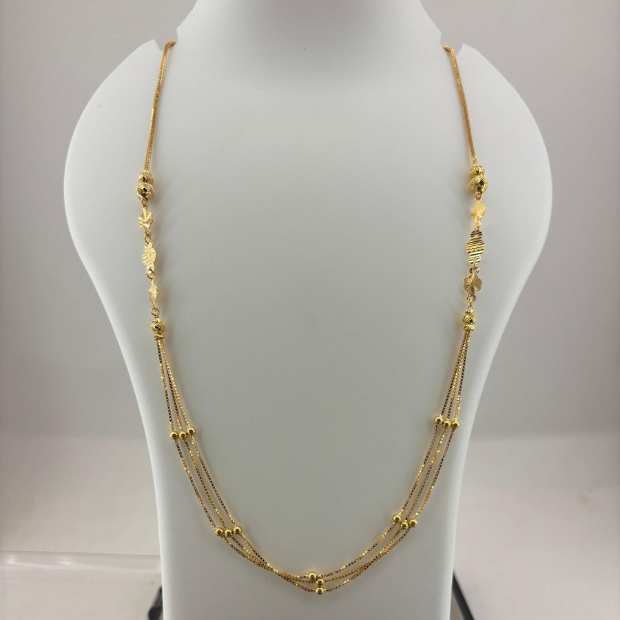 A gold multi-strand necklace displayed on a white mannequin bust, with a digital scale visible underneath. The necklace features multiple layers of chain with small gold bead and textured details.