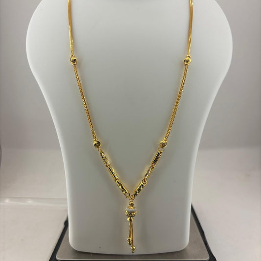 A gold necklace displayed on a white mannequin bust, with a digital scale visible underneath. The necklace features a delicate chain with small bead details and a central pendant with a vertical drop.