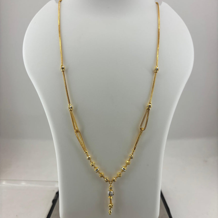 A gold necklace displayed on a white jewelry bust, with a digital scale visible underneath. The necklace features a delicate chain with small bead details and a central pendant with a clear stone.