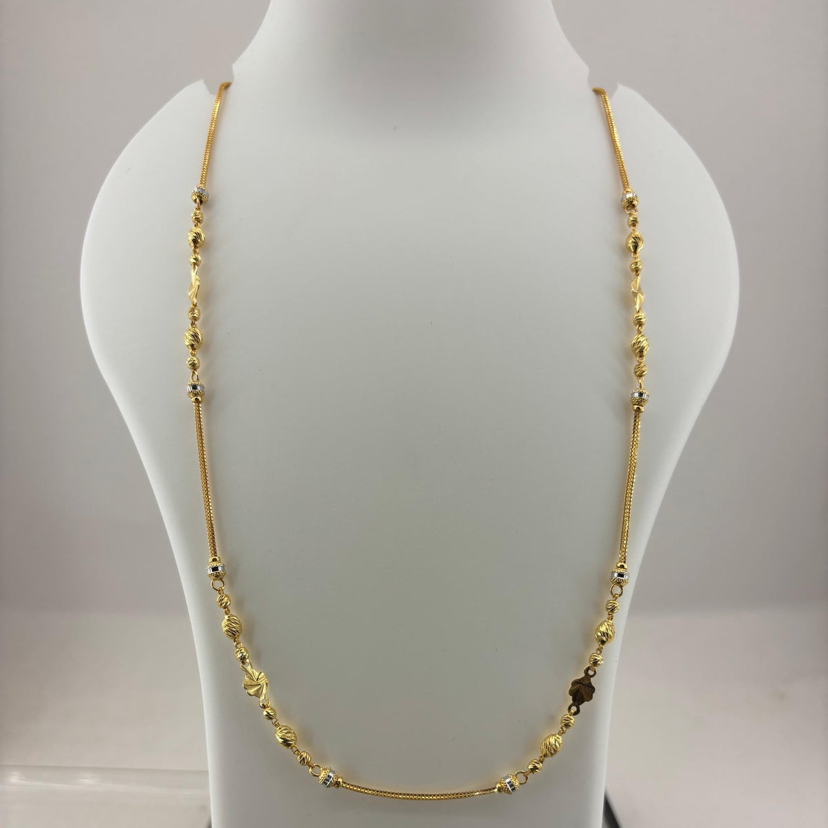 A gold-toned beaded necklace displayed on a white mannequin bust, with a digital scale visible underneath.