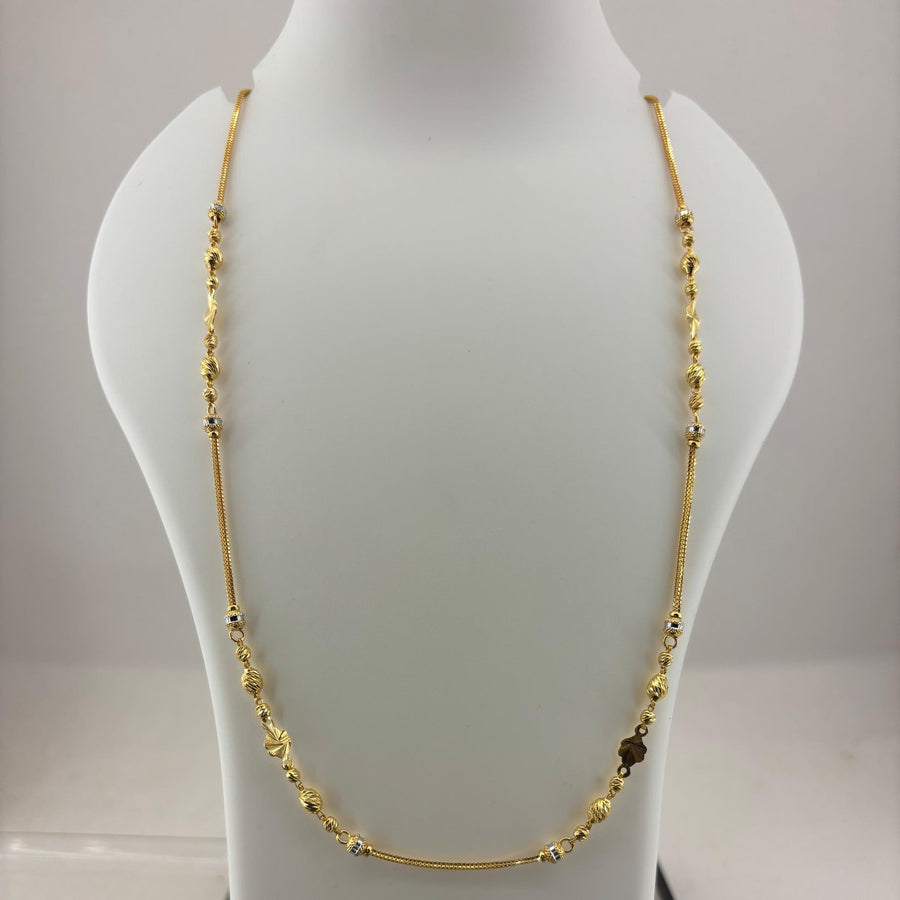 A gold-toned beaded necklace displayed on a white mannequin bust, with a digital scale visible underneath.