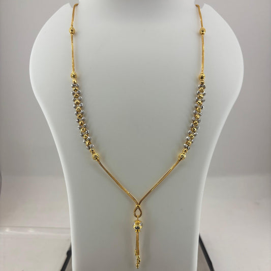 A gold-tone necklace displayed on a white mannequin bust, with a digital scale visible underneath to show the weight. The necklace features a Y-shaped design with one side in textured chain links and the other in a smoother chain, ending in a small dangling pendant.