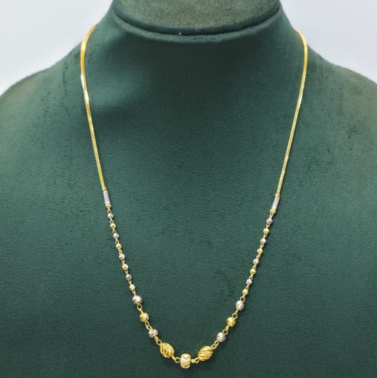 A delicate gold chain necklace with small alternating gold and white beads, featuring a central gold medallion, displayed on a dark green jewelry bust.