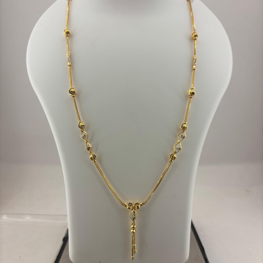 A gold necklace displayed on a white jewelry bust, with a digital scale visible underneath. The necklace features a delicate chain with small gold beads and a central pendant.