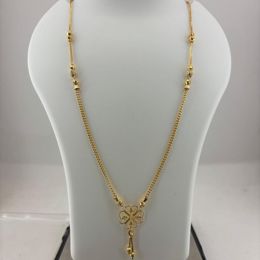 A gold necklace with a four-leaf clover pendant displayed on a white mannequin bust, with a digital scale visible underneath.