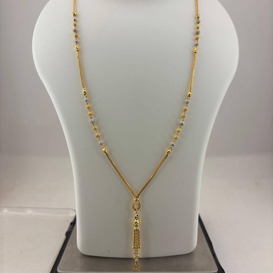 A gold necklace displayed on a white mannequin bust, with a digital scale visible underneath. The necklace features a delicate chain with small bead-like details and a textured pendant.