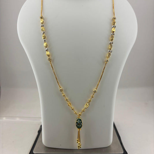 A gold necklace displayed on a white mannequin bust, with a small dark green oval pendant and gold tassel, shown resting on a digital scale.
