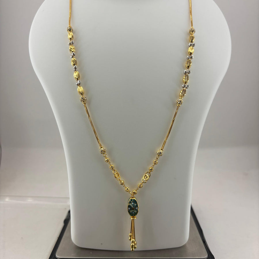 A gold necklace displayed on a white mannequin bust, with a small dark green oval pendant and gold tassel, shown resting on a digital scale.