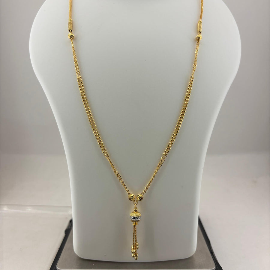 A gold-toned chain necklace with a decorative pendant is displayed on a white mannequin bust, with a digital scale visible underneath.