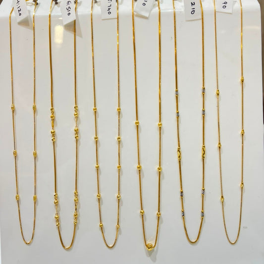 Nine gold beaded chains of varying lengths displayed on a white stand, each with a small white price tag attached.