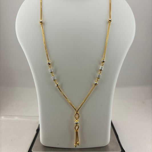 A gold chain necklace with small clear beads and a dangling gold tassel pendant, displayed on a white mannequin bust resting on a digital scale.