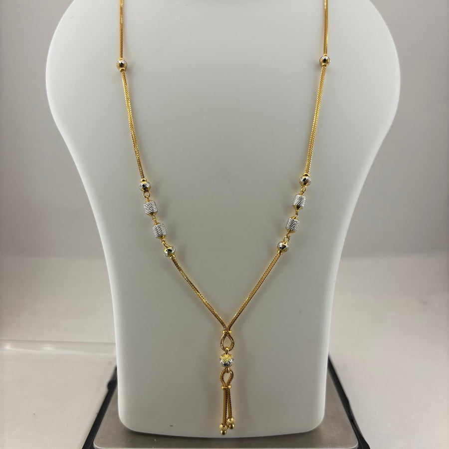 A gold chain necklace with small clear beads and a dangling gold tassel pendant, displayed on a white mannequin bust resting on a digital scale.