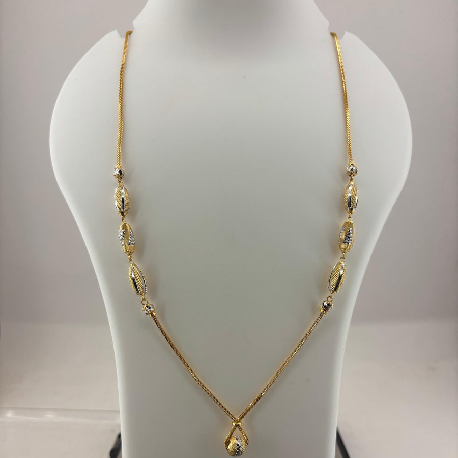 A gold necklace displayed on a white mannequin bust, with a digital scale visible underneath. The necklace features a delicate chain with elongated oval links and a teardrop-shaped pendant at the center.