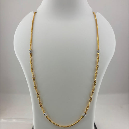 A gold chain necklace displayed on a white mannequin bust, with a digital scale visible underneath. The necklace has small silver-toned bead accents spaced along the chain.