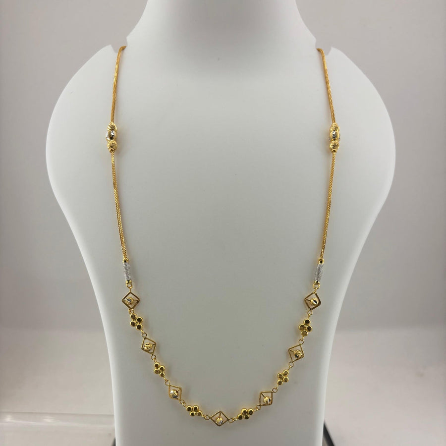 A gold chain necklace with small diamond-shaped and floral motifs displayed on a white mannequin bust, with a digital scale visible underneath.