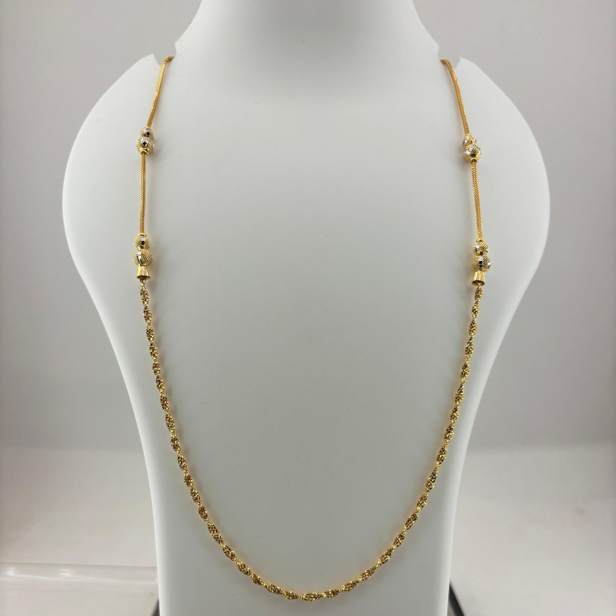 A gold chain necklace with small bead-like links and decorative spacer beads, displayed on a white jewelry bust. The bust is placed on top of a digital scale showing a weight of 8.