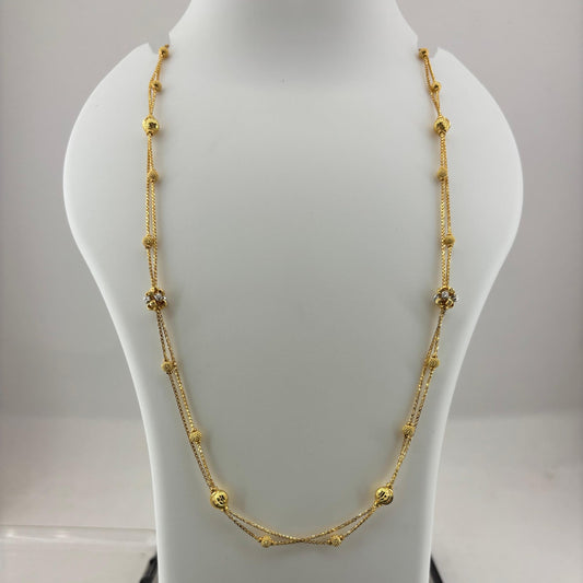 A gold necklace with small bead-like links and a central crisscross design, displayed on a white jewelry bust above a digital scale.