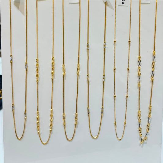 Nine gold-toned chain necklaces with various link patterns are displayed on a white vertical stand, each with a small price tag attached.