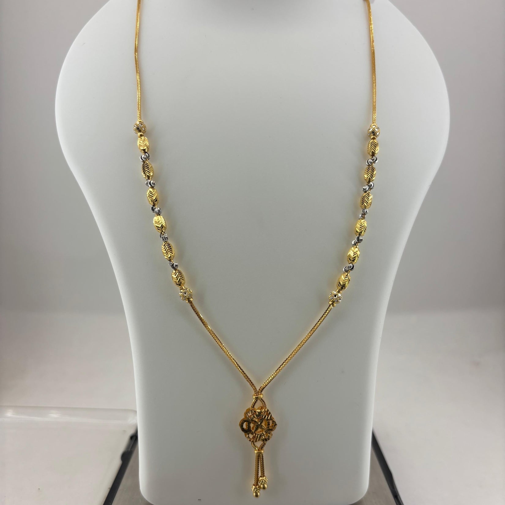 A gold necklace with a key-shaped pendant displayed on a white mannequin bust, with a digital scale visible underneath.