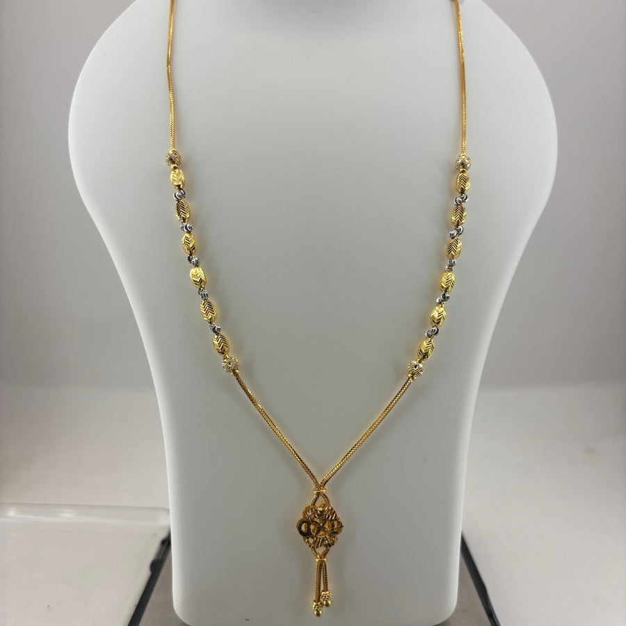A gold necklace with a key-shaped pendant displayed on a white mannequin bust, with a digital scale visible underneath.