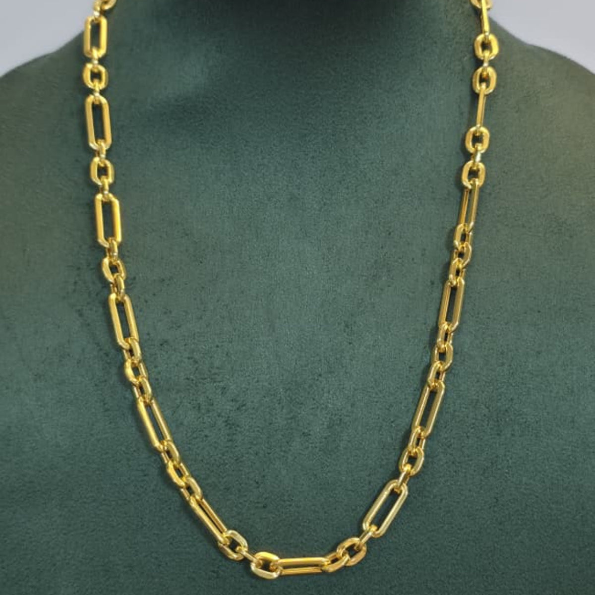 A gold chain necklace with elongated oval links displayed on a dark green jewelry bust against a light gray background.