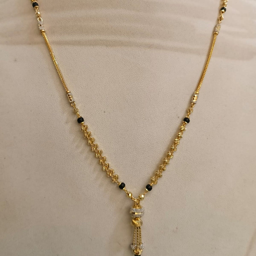 Gold chain necklace with small black bead accents and a dangling tassel pendant, displayed on a beige mannequin bust.