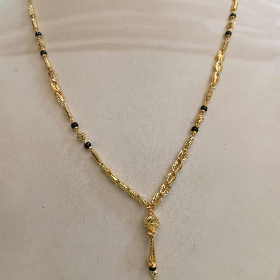 A gold necklace with small black bead accents displayed on a cream-colored mannequin bust.