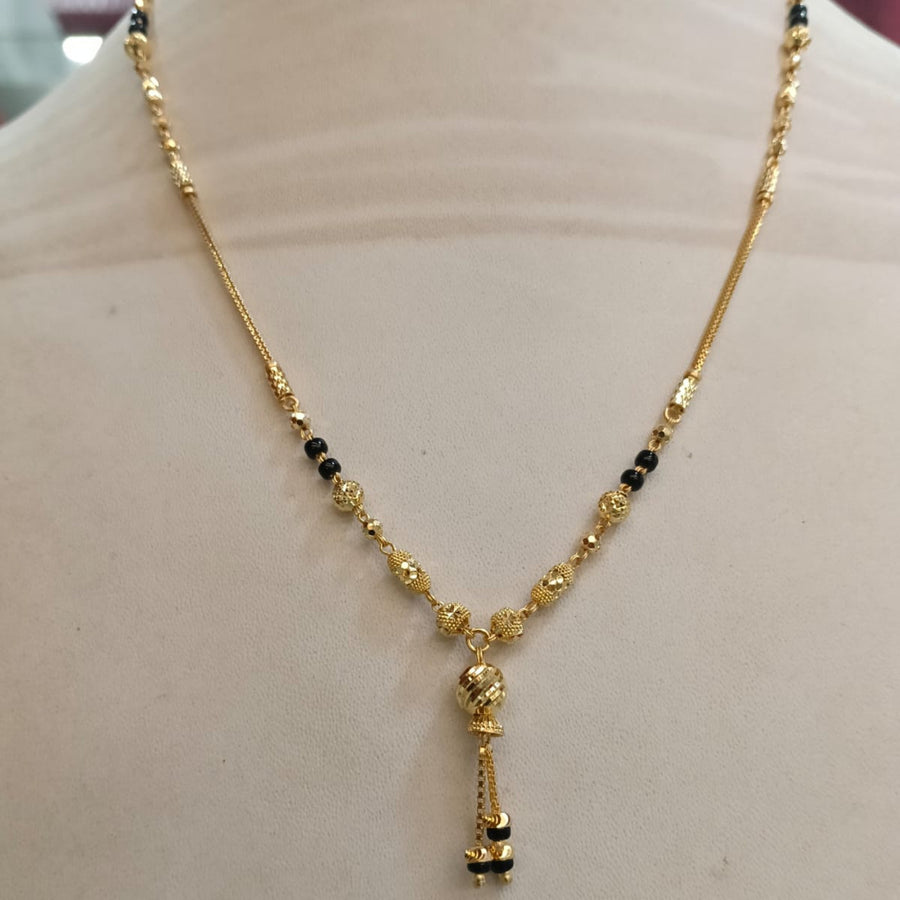 Gold necklace with small black bead accents and a dangling pendant, displayed on a beige mannequin bust.