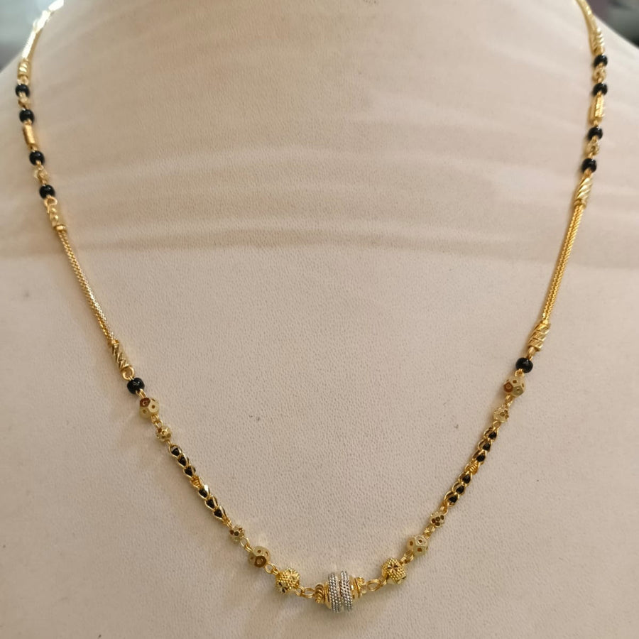 A gold chain necklace with small black bead accents and a central silver-toned pavé stone, displayed on a beige jewelry bust.