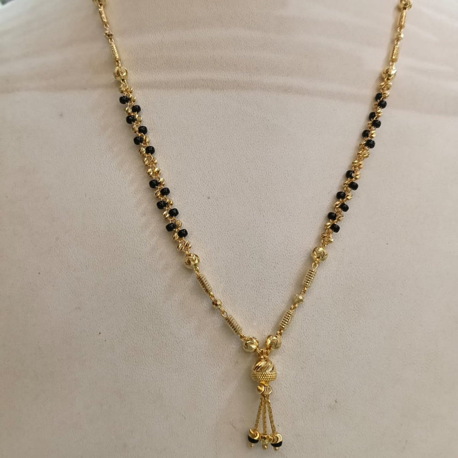 Gold necklace with black bead accents and a small dangling tassel charm, displayed on a cream-colored mannequin bust.