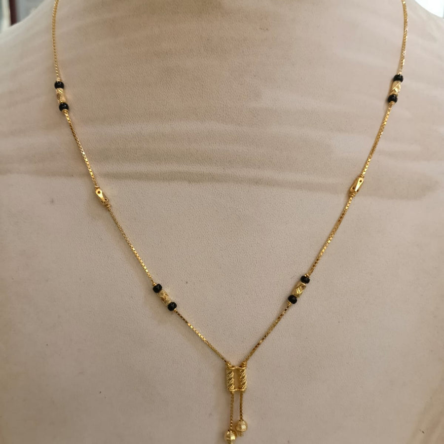 A gold chain necklace with small black beads and a textured gold pendant, displayed on a beige mannequin bust.