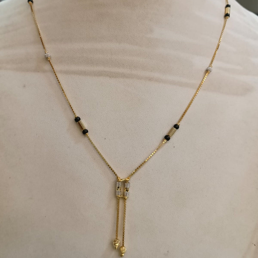 A delicate gold chain necklace displayed on a beige mannequin bust. The necklace features small black beads spaced along the chain and a central rectangular gold pendant with a dangling chain tail ending in a small gold bead.