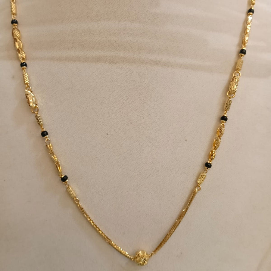A gold chain necklace with small black beads and decorative gold spacer elements, displayed on a cream-colored mannequin bust.