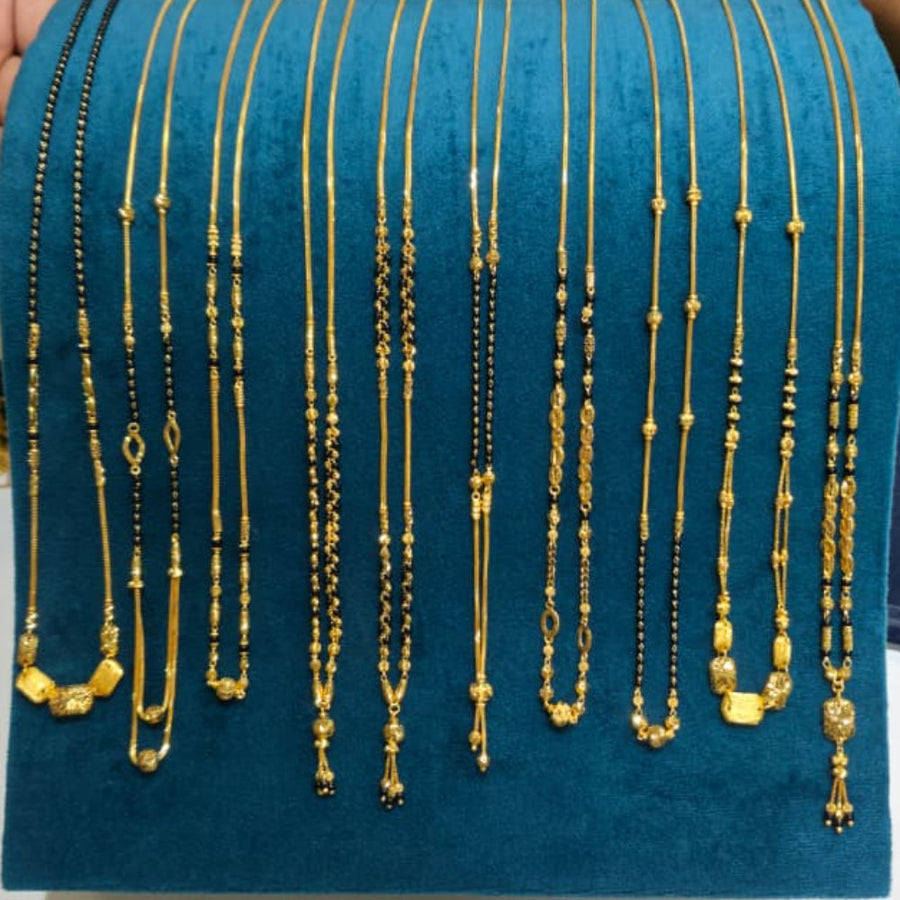 A display of multiple gold necklaces with various bead and pendant designs, arranged on a teal velvet jewelry stand. A hand is visible on the left holding the stand, and a person in a blue striped shirt is partially visible on the right.