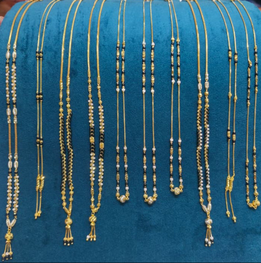 A display of multiple gold-toned beaded necklaces and chains hanging on a teal velvet jewelry stand, with hands and a workspace visible in the background.