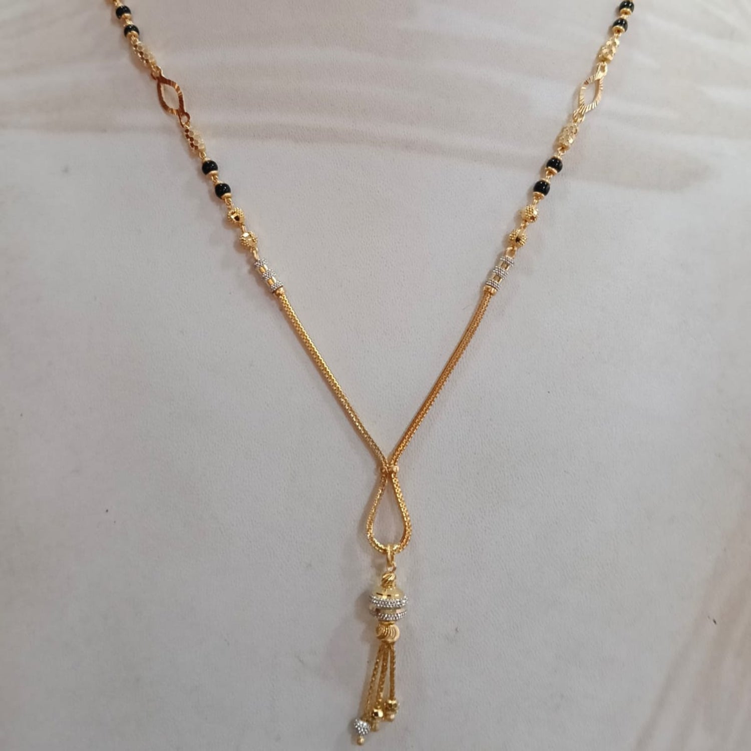 A gold-toned beaded necklace with black and white beads, displayed on a white mannequin bust.