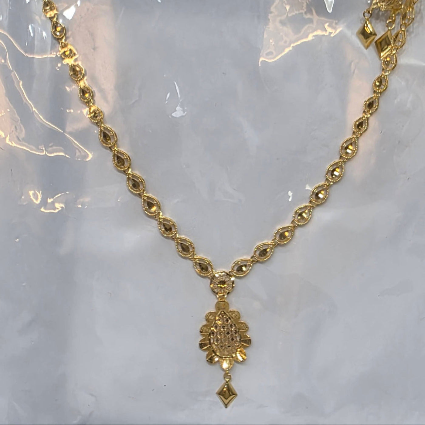 Gold necklace with a pendant on a clear plastic background