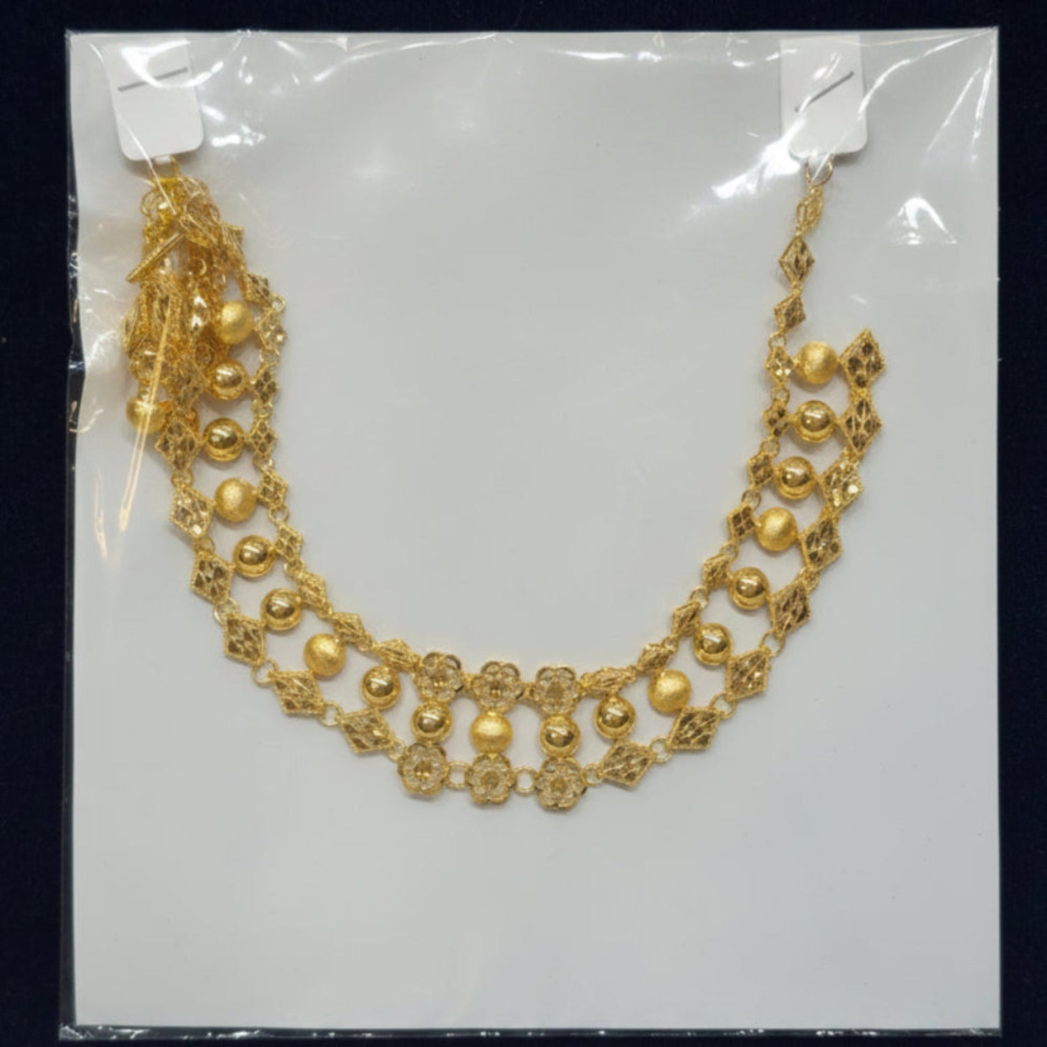 Gold necklace on a clear plastic sheet with a label, against a dark background